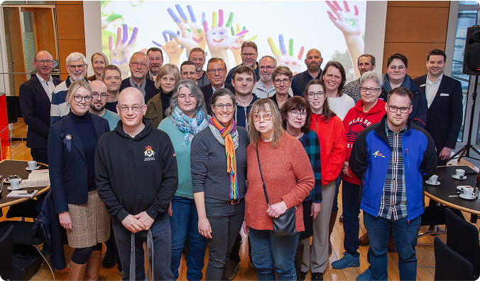 Eine Gruppe von Menschen steht in einer Reihe vor einer Leinwand mit bunten Kinderhandabdrücken.